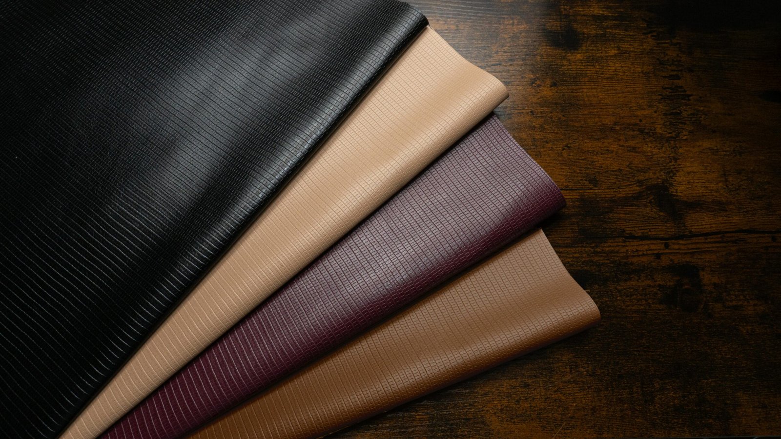 High-quality textured leather fabrics in various colors on a rustic wooden surface.